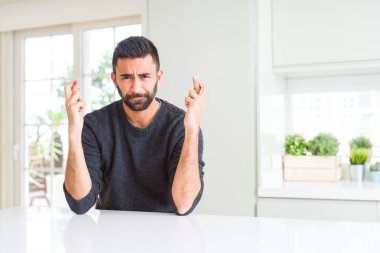 Yakışıklı İspanyol adam evde rahat kazak giyen umut ve gözleri kapalı ile geçiş parmakları gülümseyerek. Şans ve batıl kavram.