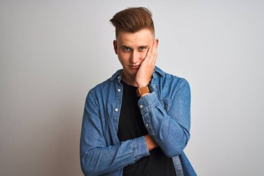 Genç yakışıklı adam izole beyaz arka plan üzerinde duran denim gömlek giyen yorgun görünümlü ve çapraz kolları ile depresyon sorunları ile sıkılmış düşünme.