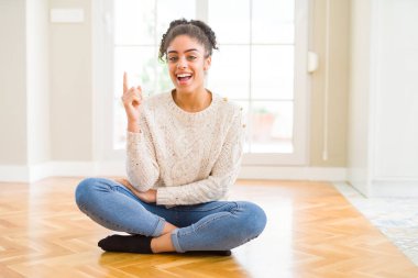 Yüzünde kocaman bir gülümseme ile katta oturan afro saçlı güzel genç Afro-Amerikan kadın kameraya bakarak yan el ve parmak ile işaret.