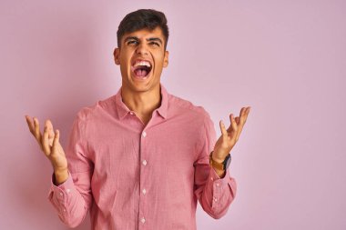 Genç hintli adam izole pembe arka plan üzerinde duran zarif gömlek deli ve deli bağırarak ve agresif ifade ve kollar kaldırdı ile bağırıyor. Hayal kırıklığı kavramı.
