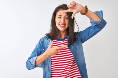 İzole beyaz arka plan üzerinde çizgili t-shirt ve kot gömlek giyen genç Çinli kadın mutlu yüz ile elleri ve parmakları ile çerçeve yapma gülümseyerek. Yaratıcılık ve fotoğrafçılık konsepti.