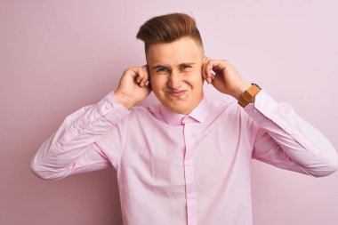 Genç yakışıklı işadamı yüksek sesle müzik sesi için rahatsız ifade ile parmakları ile kulakları kapsayan izole pembe arka plan üzerinde duran zarif gömlek giyiyor. Sağır kavramı.
