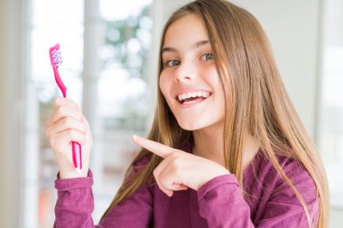 Güzel genç kız çocuk tutan pembe diş diş fırçası çok mutlu el ve parmak ile işaret