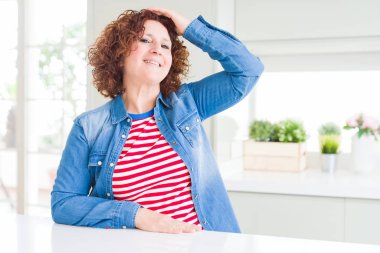 Evde kot ceket giyen kıvırcık saçlı orta yaş yaşlı kadın el kadar jest ile emin dokunmadan saç gülümseyerek, çekici ve şık poz