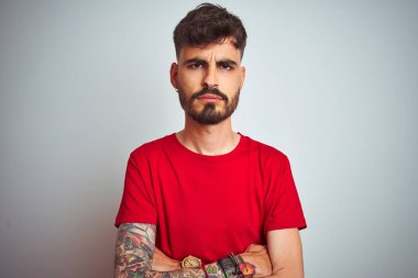 Kırmızı t-shirt giyen dövme giyen genç adam izole beyaz arka plan şüpheci ve sinir üzerinde duran, çapraz kolları ile yüzünde onaylamayan ifade. Negatif kişi.