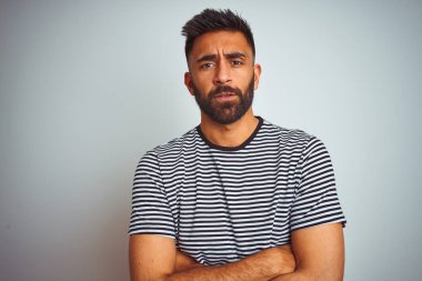 Siyah çizgili t-shirt giyen genç hintli adam izole beyaz arka plan üzerinde duran şüpheci ve sinirli, çapraz kolları ile yüzünde onaylamayan ifade. Negatif kişi.