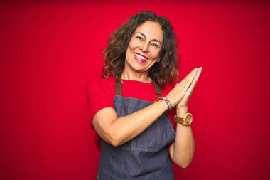 Orta yaş yaşlı kadın kırmızı izole arka plan alkışlama üzerinde önlük üniforma giyen ve mutlu ve neşeli alkışlayan, birlikte gururlu eller gülümseyen