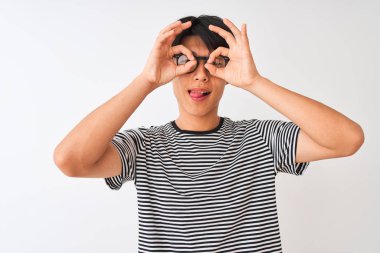 Gözlük takan Çinli adam ve izole beyaz arka plan üzerinde duran lacivert çizgili t-shirt dürbün dil dışarı yapışmasını gibi ok jest yapıyor, gözleri parmaklardan bakarak. Çılgın ifade.
