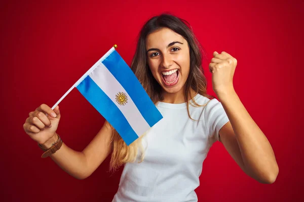 赤い孤立した背景の上にアルゼンチンの旗を持つ若い美しい女性は誇りを叫び 勝利と成功を祝う非常に興奮し 応援の感情 — ストック写真