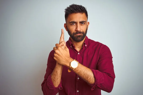 Young indian man wearing red elegant shirt standing over isolated grey background Holding symbolic gun with hand gesture, playing killing shooting weapons, angry face
