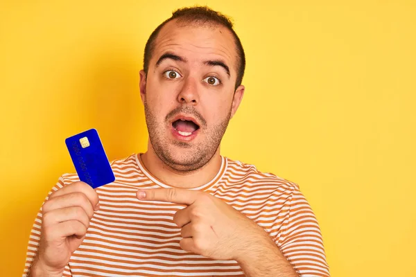 Young Man Holding Blue Credit Card Standing Isolated Yellow Background — Stock Photo, Image