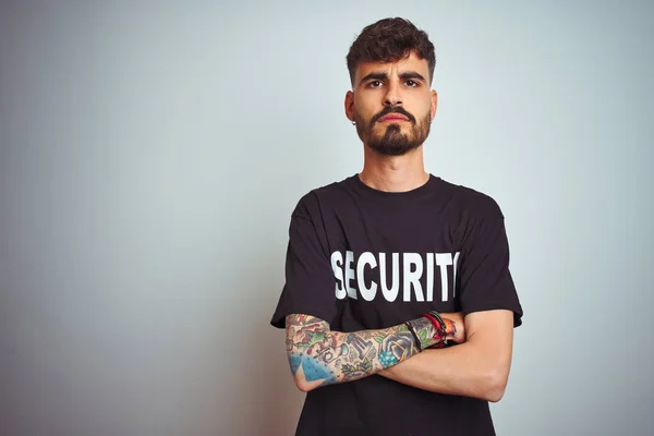 Young safeguard man with tattoo wering security uniform over isolated white background skeptic and nervous, disapproving expression on face with crossed arms. Negative person.