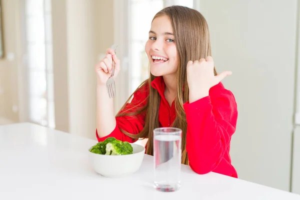 新鮮なブロッコリーを食べ 水を飲んで幸せな顔で横に親指で見せる美しい若い女の子 — ストック写真