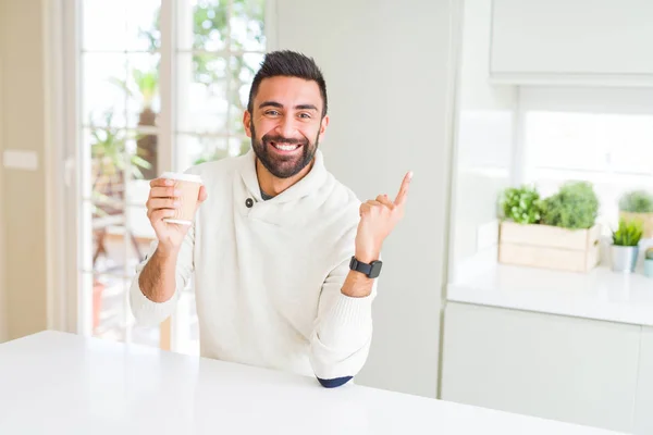 紙コップでコーヒーを飲むハンサムなヒスパニックの男は 手と指を横に指差して非常に幸せ — ストック写真