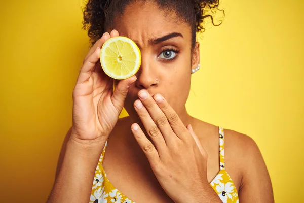 孤立した黄色の背景カバー口の上にレモンのスライスを保持する若いアフリカ系アメリカ人女性は 間違い 恐怖の表現 沈黙で怖がって 秘密の概念でショックを受けた手で口を覆う — ストック写真