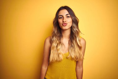 Genç güzel kadın sarı izole arka plan üzerinde t-shirt giyen kamera hava güzel ve seksi olmak bir öpücük üfleme bakarak. Aşk ifadesi.