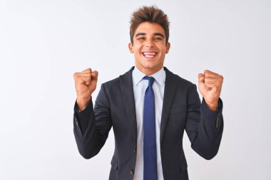 İzole beyaz arka plan üzerinde duran takım elbise giyen genç yakışıklı işadamı kollarını kaldırdı ve gözleri açık başarı için şaşırttı. Kazanan kavramı.