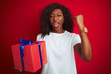 Genç afro-amerikan kadın izole kırmızı arka plan üzerinde ayakta tutan kızgın ve sinirli öfke ile bağırarak, deli ve yükseltilmiş el, öfke kavramı ile bağırıyor