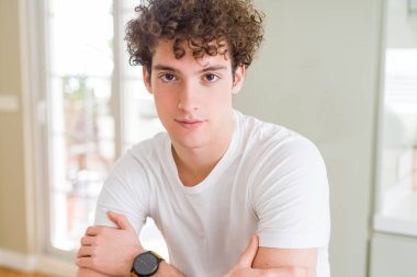 Yüzünde ciddi bir ifade ile beyaz t-shirt gevşek giyen genç yakışıklı adam. Basit ve çapraz silah ile doğal