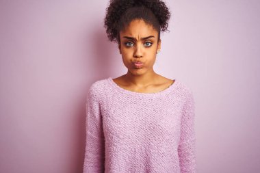 Genç afro-amerikan kadın komik yüzü ile izole pembe arka plan üzerinde duran kış kazak giyiyor yanaklar şişirme. Ağız hava ile şişirilmiş, deli ifade.