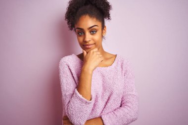 Kışlık kazak giyen genç afro-amerikan kadın izole pembe arka plan üzerinde duran kamera emin bakarak çapraz kolları ve çene üzerinde kaldırdı ile gülümseyerek. Olumlu düşünme.