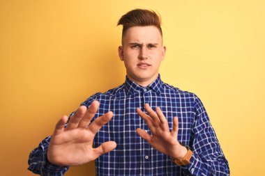 Izole sarı arka plan üzerinde duran rahat gömlek giyen genç yakışıklı adam iğrenmiş ifade, hoşnutsuz ve korkulu tiksinti yüz yapıyor çünkü nefret tepki. Elleri havada. Sinir bozucu kavram.