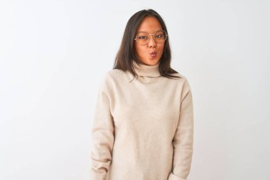 Genç Çinli kadın boğazlı kazak ve gözlük giyen izole beyaz arka plan dudaklar, deli ve komik jest ile balık yüz yapma. Komik ifade.