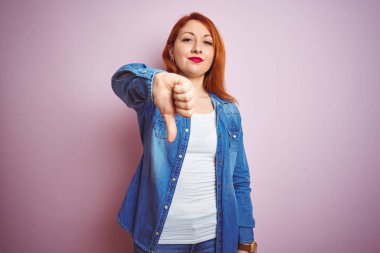 Youg güzel kızıl saçlı kadın izole pembe arka plan üzerinde duran denim gömlek giyen mutsuz ve kızgın gösteren reddi gösteren ve başparmak aşağı jest ile negatif. Kötü ifade.