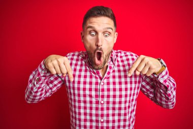 Kırmızı izole arka plan üzerinde genç yakışıklı adam reklam gösteren parmakları ile aşağı işaret, sürpriz yüz ve açık ağız