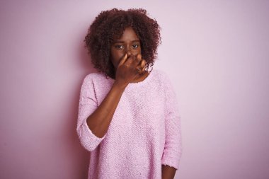 Genç afrikalı afro kadın izole pembe arka plan üzerinde duran kazak giyen bir şey kokulu ve, dayanılmaz koku, burun parmakları ile nefes tutarak. Kötü kokular kavramı.