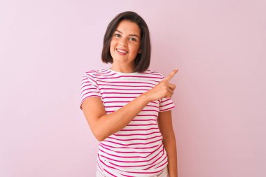Genç güzel kadın çizgili t-shirt izole pembe arka plan neşeli üzerinde duran bir gülümseme ile yüz işaret el ve parmak ile yan kadar mutlu ve doğal ifade ile