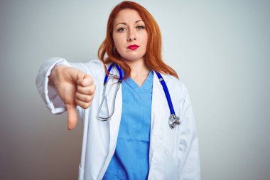 Genç kızıl saçlı doktor kadın beyaz izole arka plan üzerinde stetoskop kullanarak mutsuz ve kızgın gösteren reddi gösteren ve başparmak aşağı jest ile negatif. Kötü ifade.