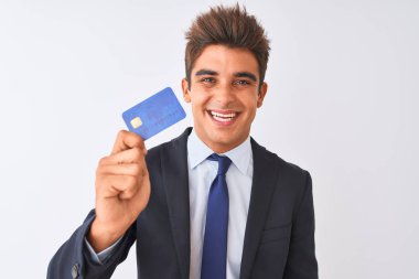 Genç yakışıklı işadamı ayakta mutlu bir yüz ile izole beyaz arka plan üzerinde kredi kartı tutan takım elbise giyen ve dişleri gösteren kendinden emin bir gülümseme ile gülümseyerek