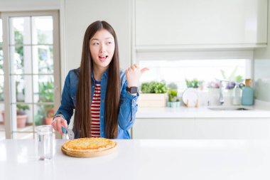 Güzel Asyalı kadın yeme ve satranç pizza kesme işaret ve mutlu yüzü gülümseyerek yan kadar başparmak ile gösteren