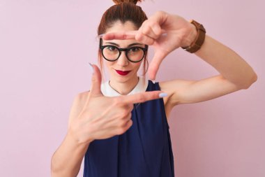 Pigtail zarif elbise ve gözlük izole pembe arka plan üzerinde giyen Redhead kadın mutlu yüz ile elleri ve parmakları ile çerçeve yapma gülümseyerek. Yaratıcılık ve fotoğrafçılık konsepti.