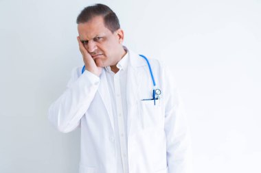 Orta yaş doktor adam beyaz arka plan üzerinde stetoskop ve tıbbi ceket giyen yorgun görünümlü ve çapraz kollar ile depresyon sorunları ile sıkılmış düşünme.