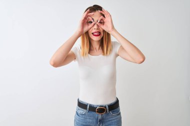 Güzel kızıl saçlı kadın rahat t-shirt izole beyaz arka plan üzerinde duran dürbün dil dışarı yapışmasını gibi ok jest yapıyor, gözleri parmaklardan bakarak. Çılgın ifade.
