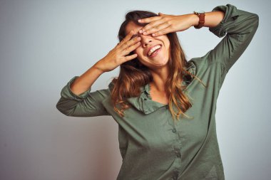 Yeşil gömlek giyen genç güzel kadın elleri neşeli ve komik gülümseyen gözleri kaplayan gri izole arka plan üzerinde duran. Kör kavramı.