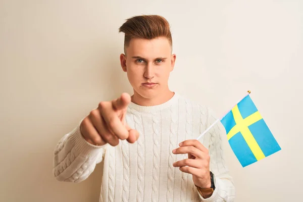 年轻的帅哥拿着瑞典Sweadish国旗在孤立的白色背景上用手指指着相机和你 手签名 积极和自信的姿态从前面 — 图库照片