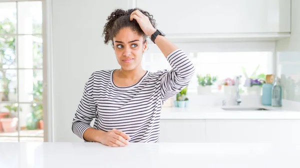 Beautiful african american woman with afro hair wearing casual striped sweater confuse and wondering about question. Uncertain with doubt, thinking with hand on head. Pensive concept.