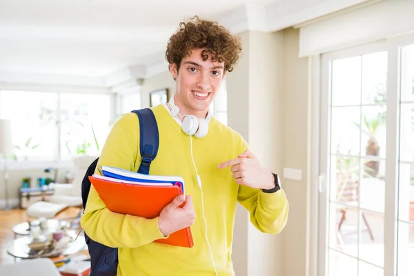 年轻的学生男子戴着耳机和背包拿着笔记本 带着惊喜的脸指着自己 — 图库照片