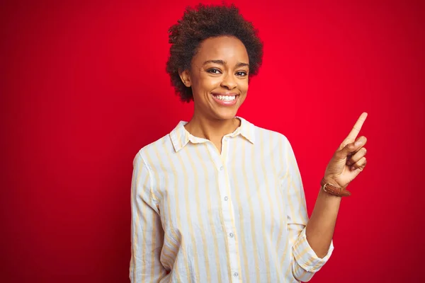 Young beautiful african american woman with afro hair over isolated red background with a big smile on face, pointing with hand and finger to the side looking at the camera.