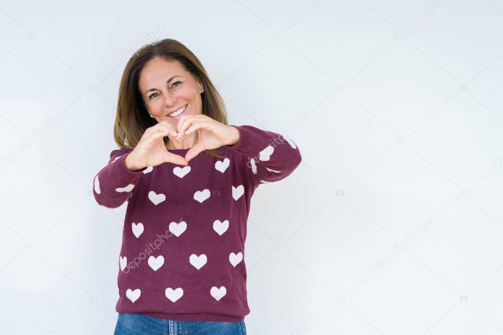 Beautiful middle age woman wearing heart sweater over isolated background smiling in love showing heart symbol and shape with hands. Romantic concept.