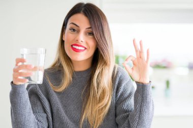 Genç güzel kadın parmakları ile ok işareti yapıyor evde su bardak içme, mükemmel sembol