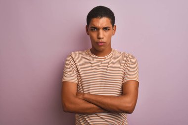 Genç yakışıklı Arap adam çizgili t-shirt izole pembe arka plan şüpheci ve sinir üzerinde duran giyen, çapraz kolları ile yüzünde onaylamayan ifade. Negatif kişi.