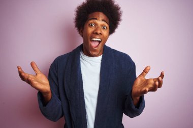 Genç afro-amerikan adam pijama giyen izole pembe arka plan üzerinde duran deli kutluyor ve kollarını kaldırdı ve açık gözleri heyecan çığlık ile başarı için hayran. Kazanan kavramı