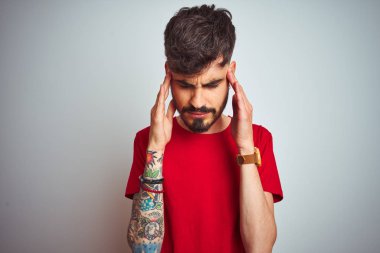 Kırmızı tişört giyen dövmeli genç adam, eliyle baş ağrısı için izole beyaz arka plan üzerinde duruyor çünkü stres. Acı çeken migren.