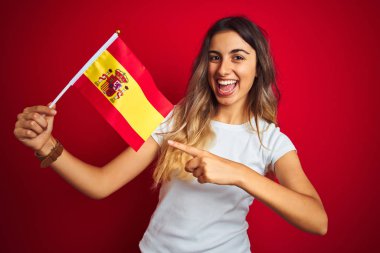 Genç güzel kadın kırmızı izole arka plan üzerinde İspanyol bayrağı tutan çok mutlu el ve parmak ile işaret