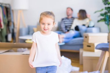 Güzel aile, anne-babalar kanepede kahve içme oturmuş karton kutular etrafında yeni evde oynayan çocuğuna bakıyor