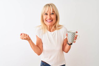 Orta yaş kadın izole beyaz arka plan üzerinde duran kahve fincan içme gurur çığlık ve zafer ve başarı çok heyecanlı kutluyor, duygu tezahürat